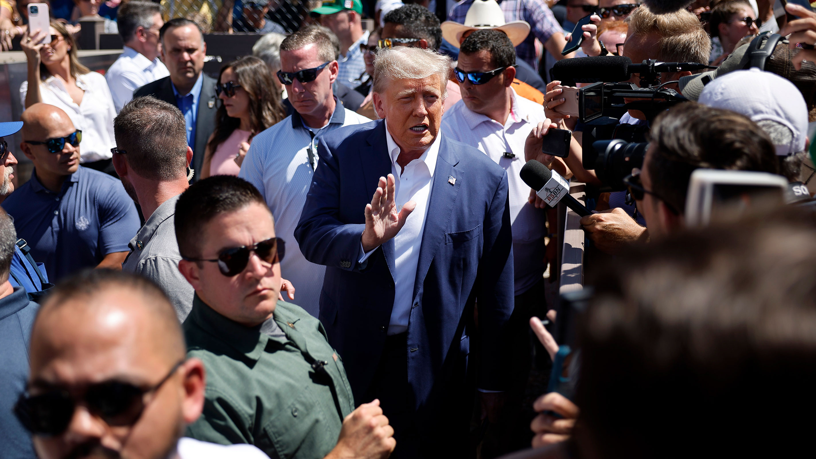 Surrounded by campaign staff and members of the US Secret Service, former President Donald Trump waves to supporters as he visits the Iowa Pork Producers Tent at the Iowa State Fair on August 12, 2023 in Des Moines, Iowa. 